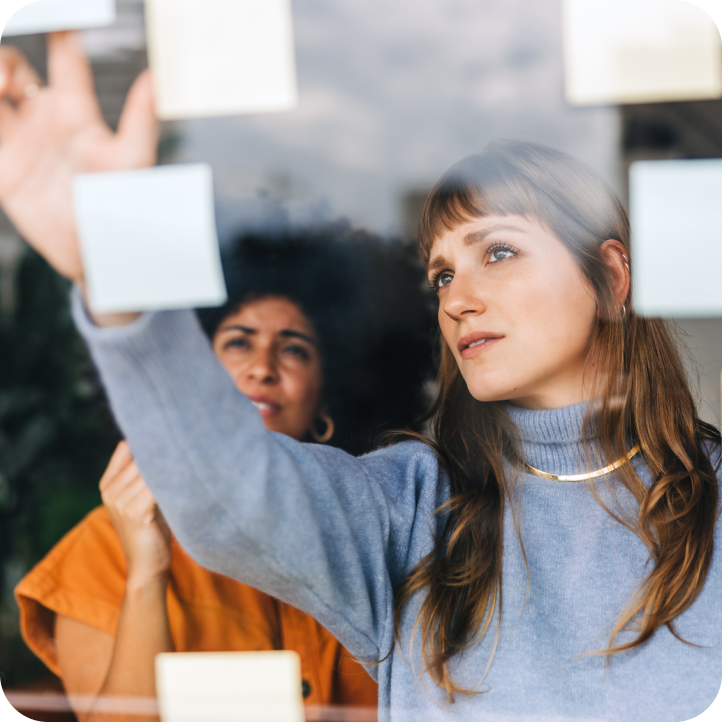 Two women brainstorming and placing sticky notes on a glass wall.