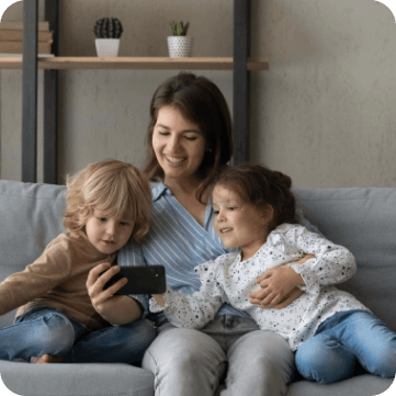 A mother sitting on a couch with her two children, watching something on a smartphone together.
