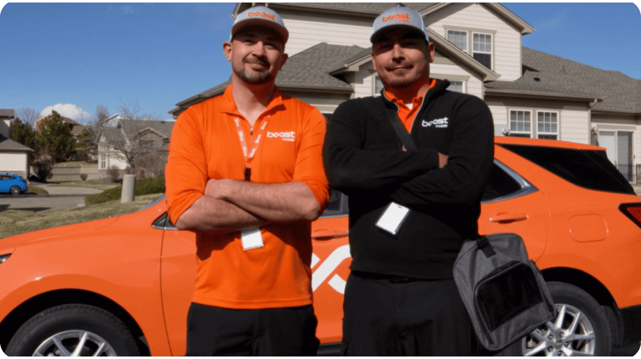 Two Boost Mobile techs standing in front of Boost orange vehicle 