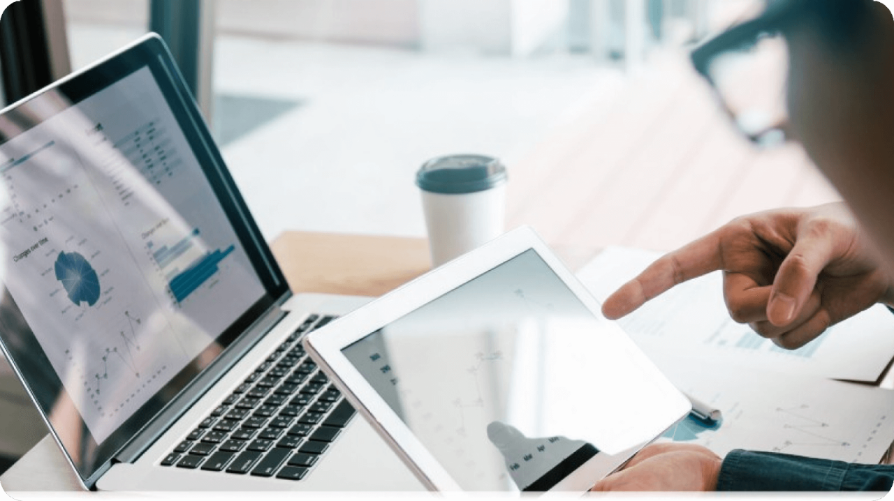 Person pointing at tablet with laptop in background.