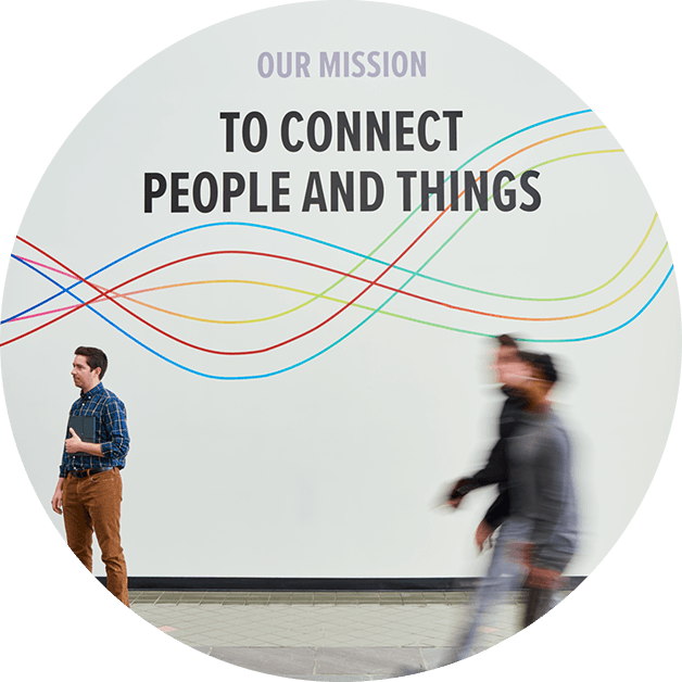 People walking in front of a wall that says "our mission: to connect people and things"
