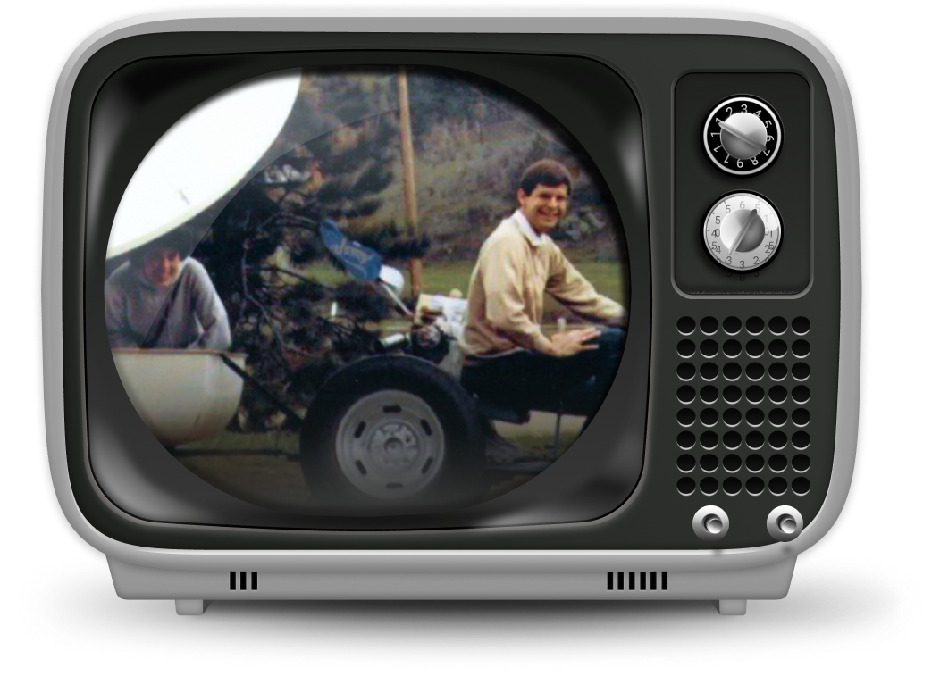 A vintage television displaying an old photo of two men working on satellite equipment outdoors.