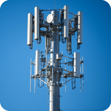 A close-up view of a telecommunications cell tower with multiple antennas against a bright blue sky.
